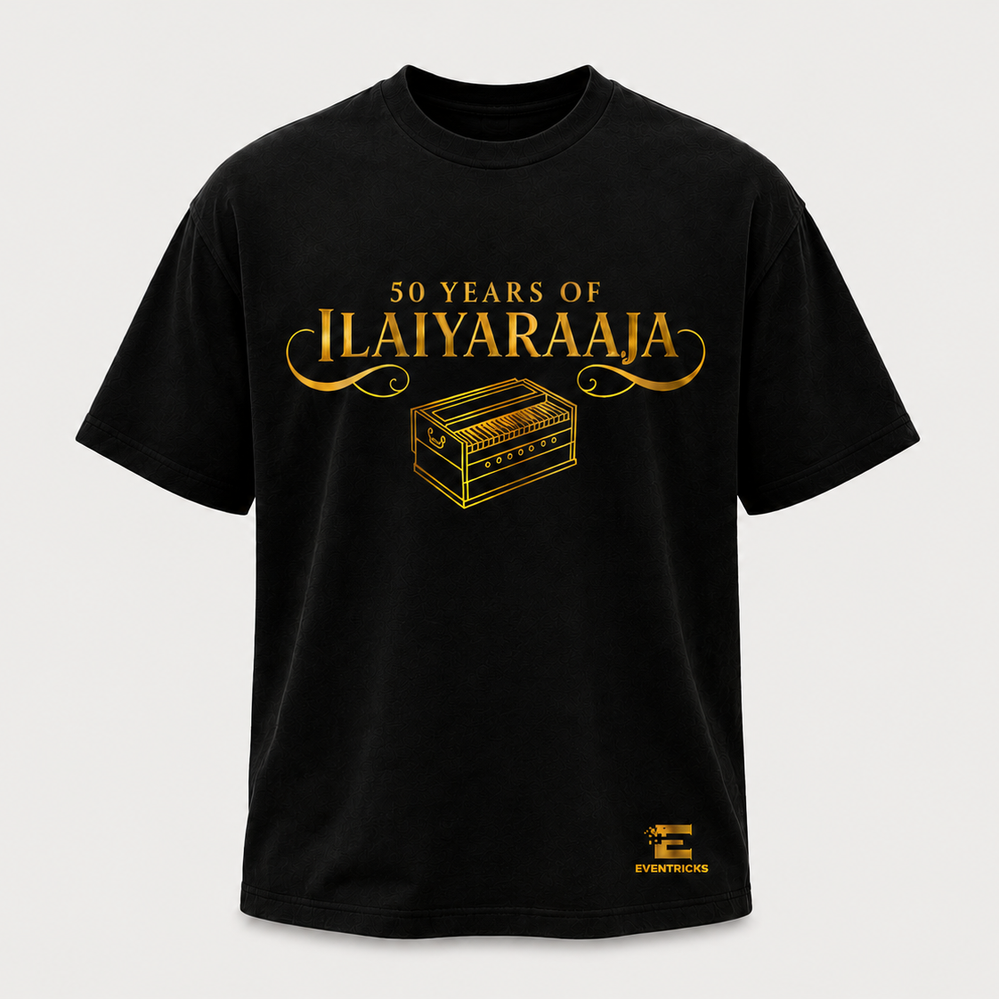 A black short-sleeve crewneck t-shirt with a gold graphic print on the front reading '50 YEARS OF ILAIYARAAJA' above an illustration of a chest, and a small gold logo near the lower right hem, shown on a light gray background.