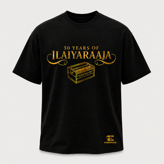 A black short-sleeve crewneck t-shirt with a gold graphic print on the front reading '50 YEARS OF ILAIYARAAJA' above an illustration of a chest, and a small gold logo near the lower right hem, shown on a light gray background.